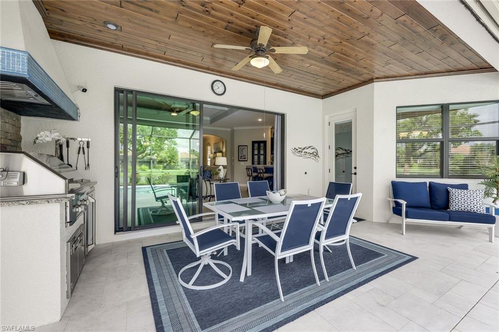 Covered lanai with a wood ceiling, outdoor dining set, built-in grill, and blue seating.