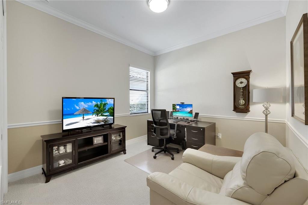 Furnished home office with a desk, television, and cream leather sofa.