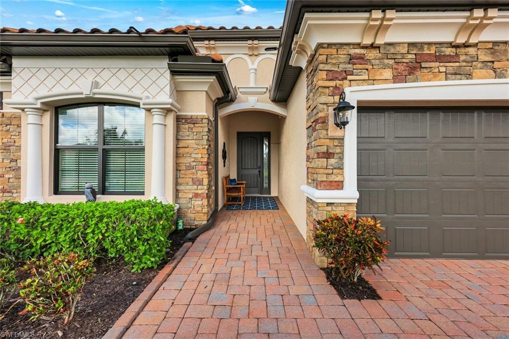 House entrance with stone accents, a brick paver walkway, and an attached gray garage door.