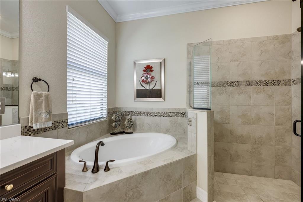 Bathroom with an oval soaking tub, tiled walk-in shower, and window with white blinds.