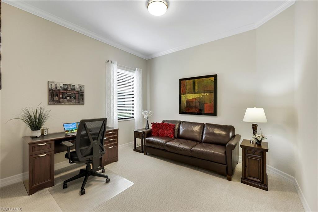 Furnished home office with a dark wood desk and brown leather sofa beside a window with white blinds.