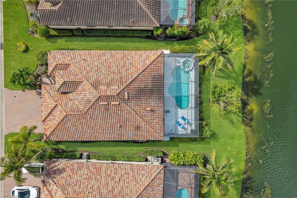 Aerial view of a tile-roofed home with a screened pool beside a canal.