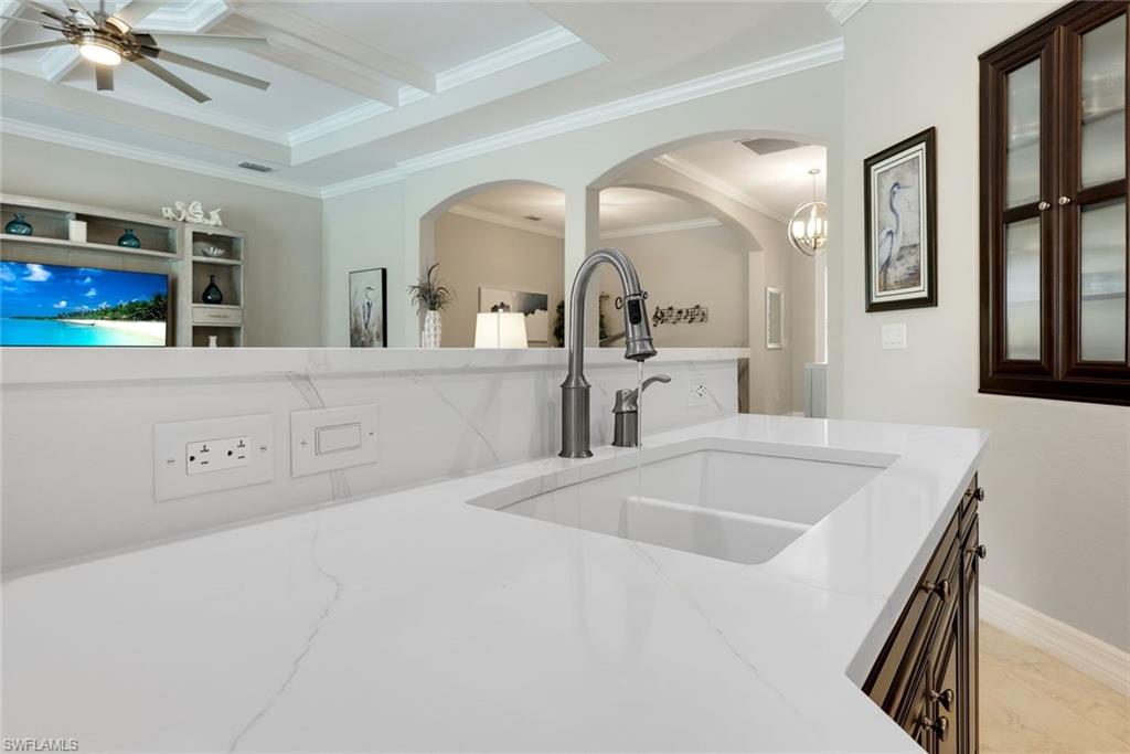 Kitchen sink and white countertop overlooking an adjoining living area through arched openings.