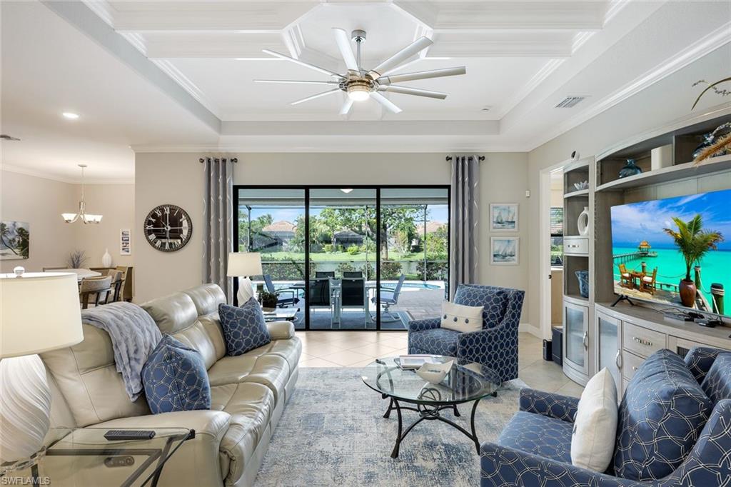 Living room with white leather sofa, blue armchairs, coffered ceiling, and sliding doors overlooking the pool.