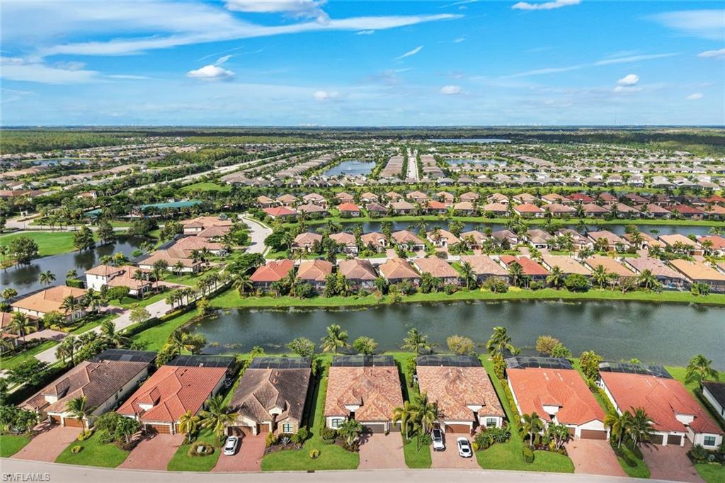 Aerial view of terracotta-roofed homes beside a pond, with palms and a residential neighborhood stretching into the distance.