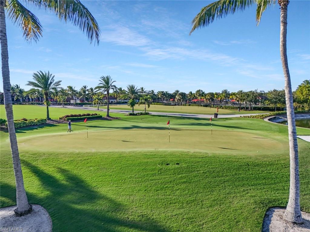 Golf course green with red flagsticks, a golfer, and palm trees.