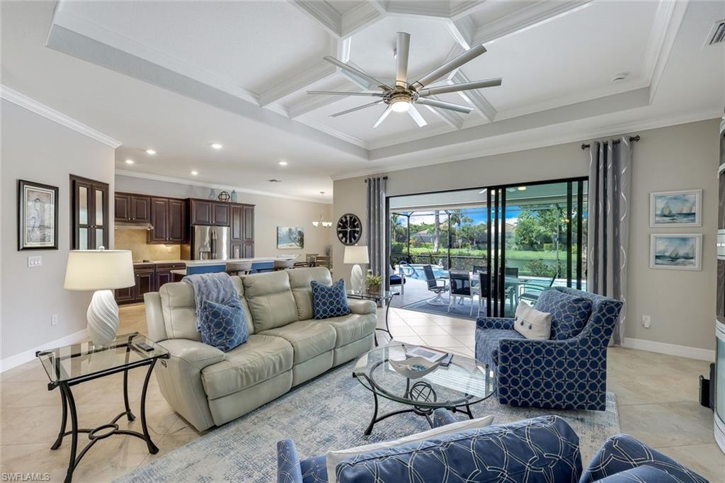 Living room with a coffered ceiling, blue accent chairs, and sliding doors to a patio and pool.