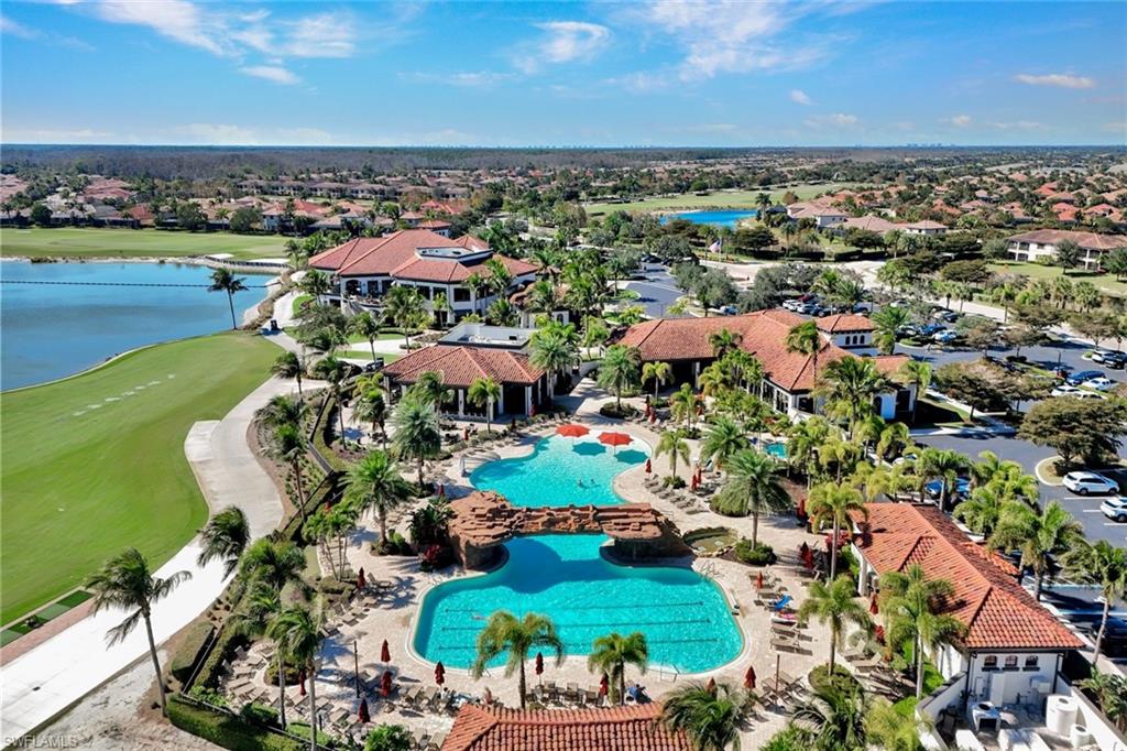 Aerial view of a community pool and clubhouse beside a lake and green space.