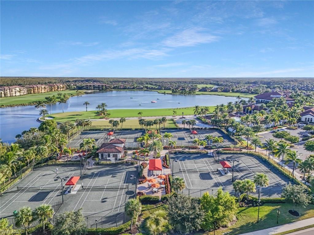 Aerial view of tennis courts beside a lake, surrounded by palm trees and homes.