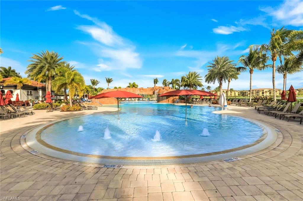 Community pool with fountains, red umbrellas, lounge chairs, and palm trees.