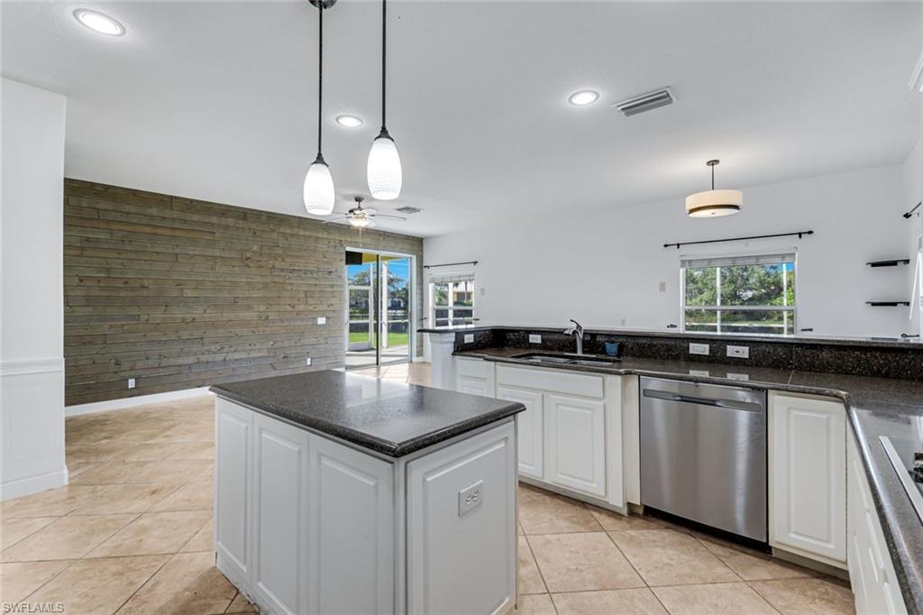 Kitchen with a central island, dark granite counters, white cabinetry, and a weathered wood accent wall.