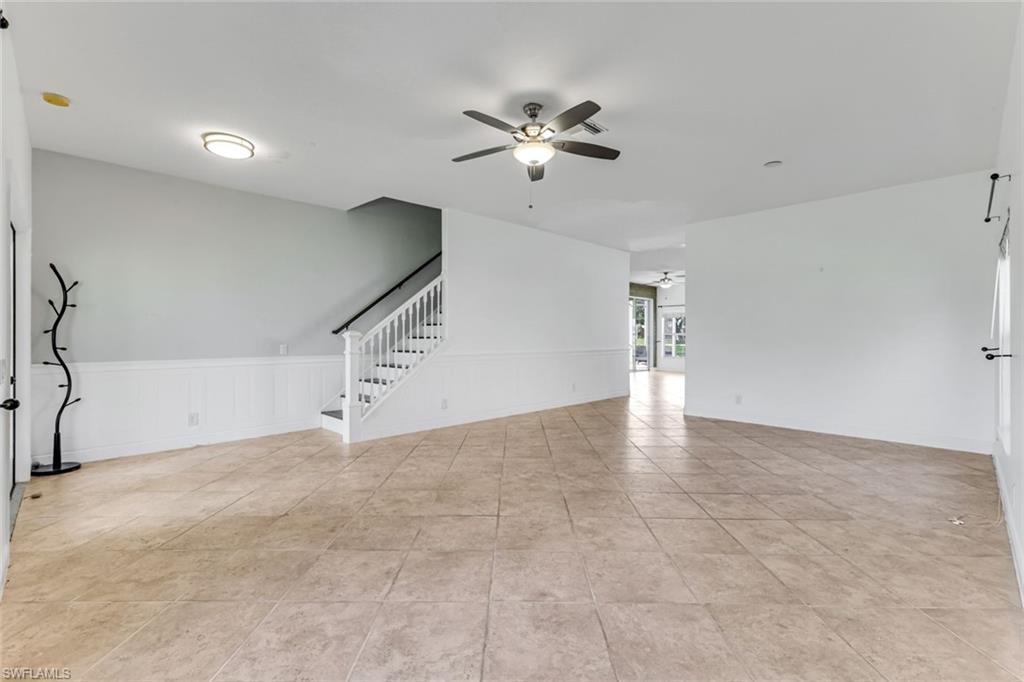 Empty living area with tiled floors, white wainscoting, and a staircase.