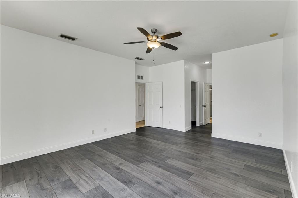 Empty room with gray plank flooring, white walls, and a ceiling fan with light.
