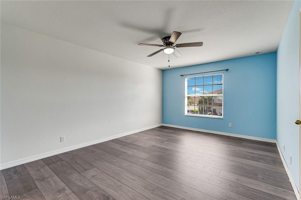 Vacant bedroom with gray plank flooring, a blue accent wall, and a ceiling fan.