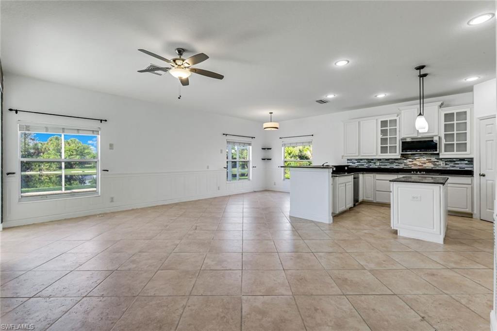 Unfurnished kitchen and dining area with white cabinetry, an island, and large windows overlooking greenery.