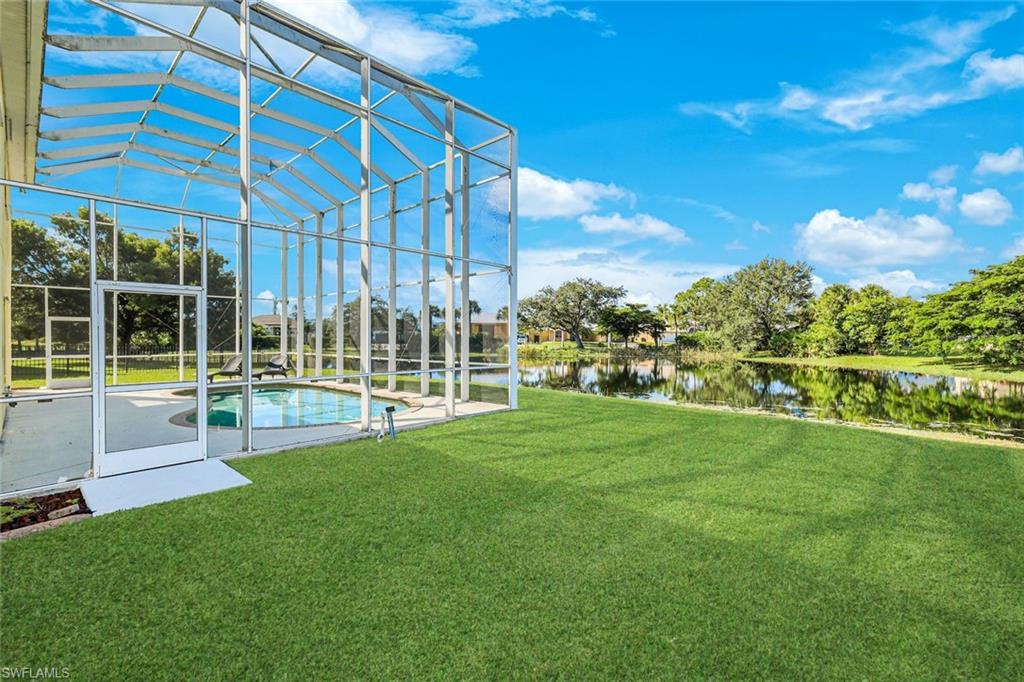 Screened backyard pool beside a broad lawn, with a tree-lined pond beyond.