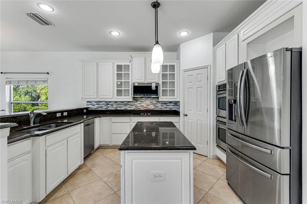 Kitchen with white cabinets, dark granite island, stainless steel appliances, and a window overlooking greenery.