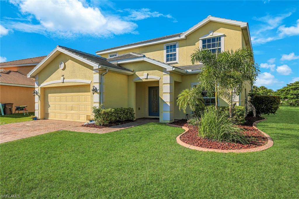 Two-story yellow home with a double garage, paver driveway, and landscaped front lawn.