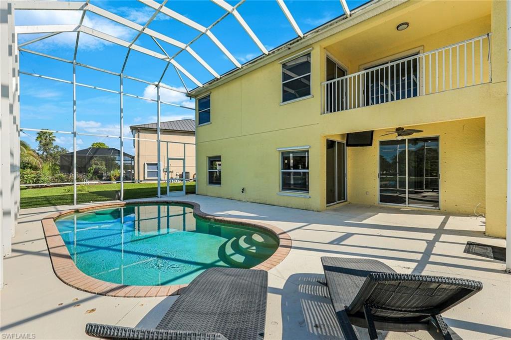 Backyard pool in a screened lanai beside a yellow two-story home with an upper balcony.