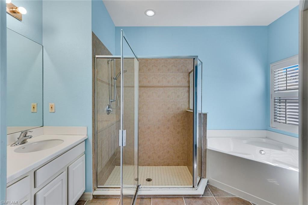 Bathroom with a glass-enclosed shower, corner soaking tub, white vanity, and light blue walls.