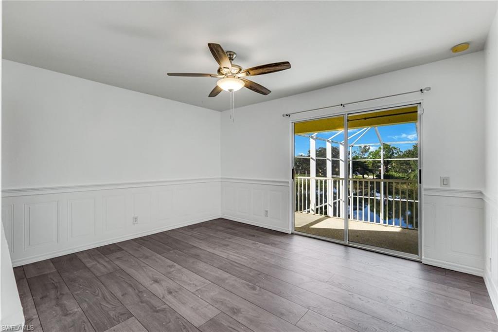 Vacant room with gray plank flooring, white wainscoting, and sliding doors overlooking water.