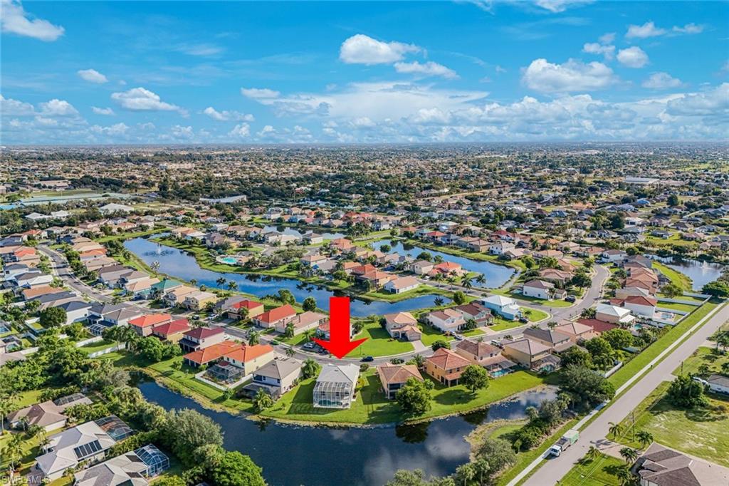 Aerial view of a canal-side Cape Coral home marked by a red arrow, surrounded by waterways and neighboring houses.