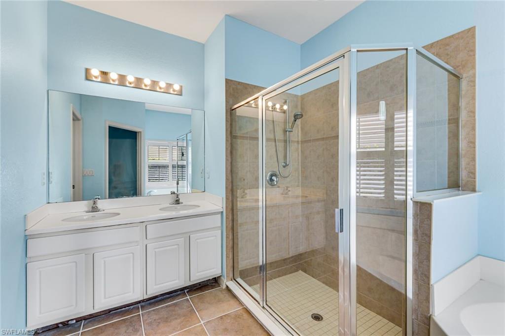 Bathroom with a white double vanity and a large glass-enclosed tan-tile shower.