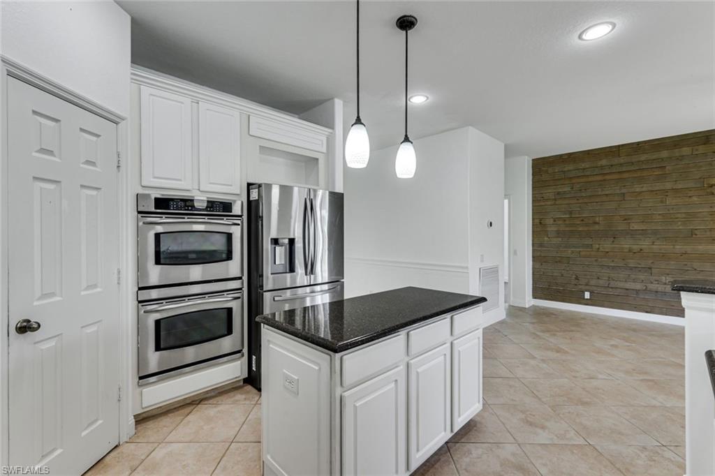 Kitchen with white cabinets, stainless steel appliances, dark island countertop, and wood-plank accent wall.