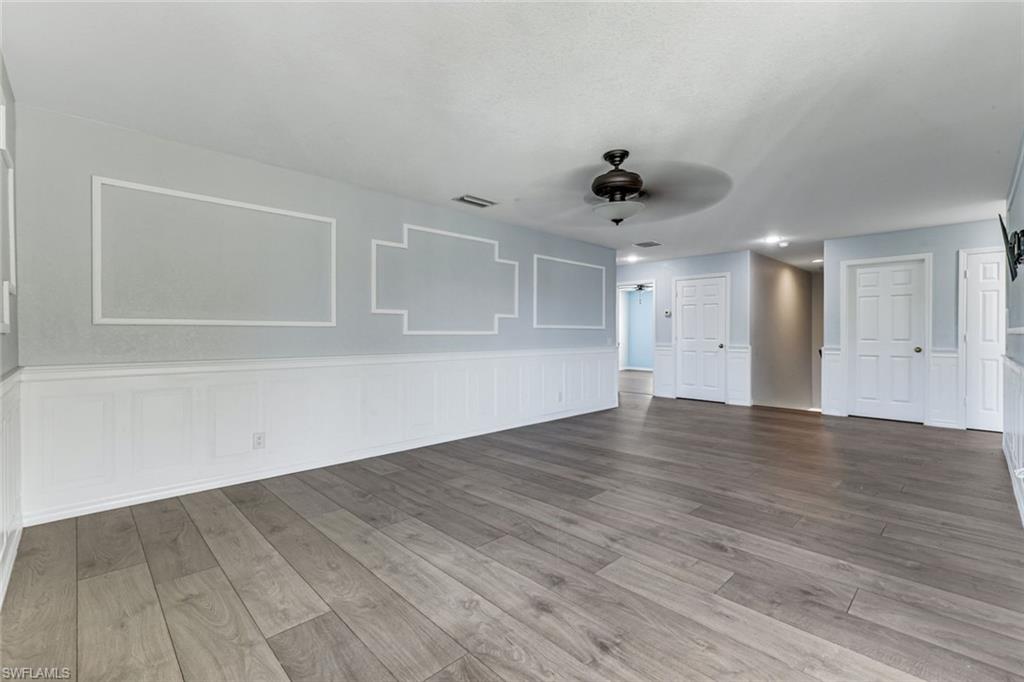 Vacant room with decorative wall molding, white wainscoting, gray tile flooring, and several doors.