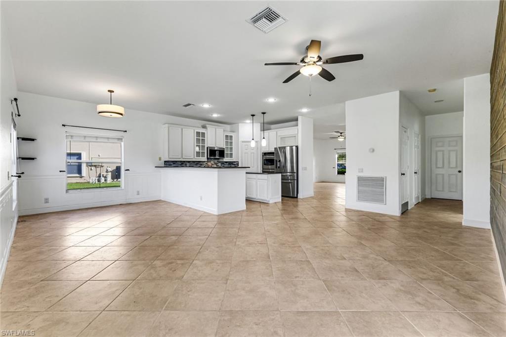 Open kitchen with white cabinets, stainless steel appliances, a breakfast bar, and beige tile floors.
