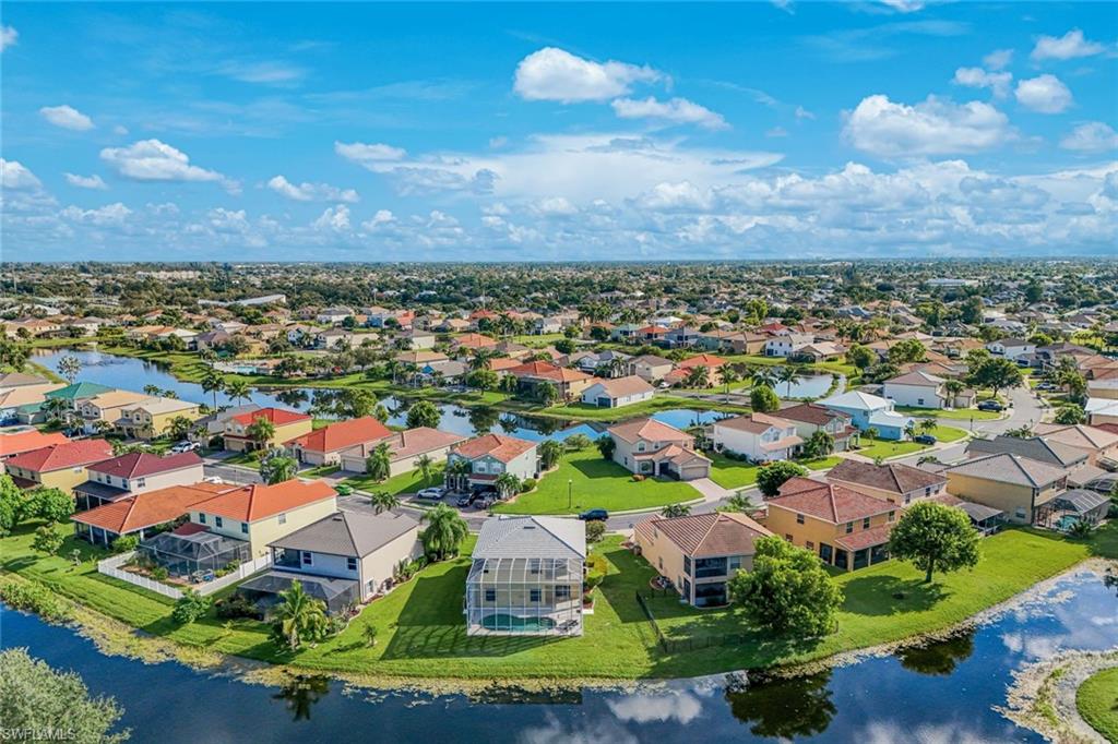Aerial view of a canal-front home amid a sunny neighborhood of homes and waterways.
