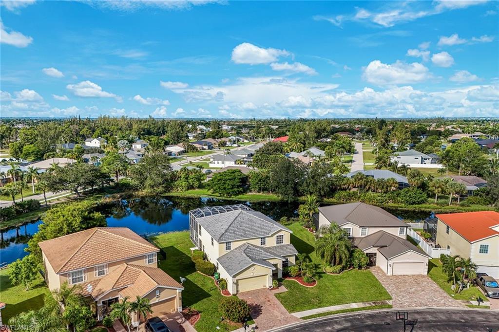 Aerial view of a Cape Coral home beside a lake, surrounded by houses and palm trees.