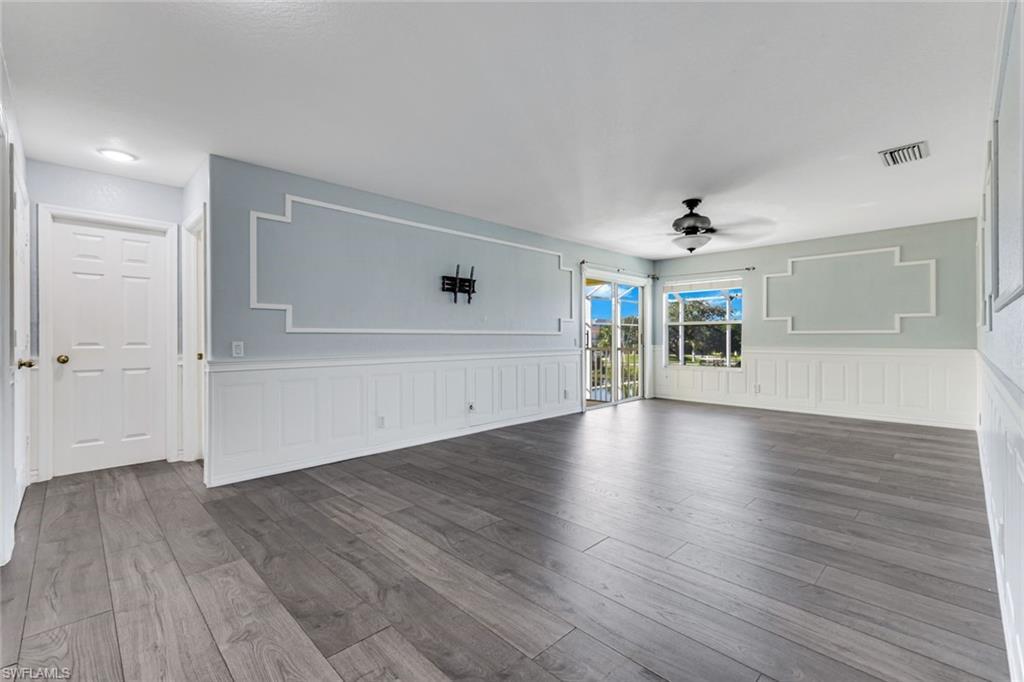 Vacant living room with gray plank floors, white wainscoting, decorative wall trim, and a sliding glass door.