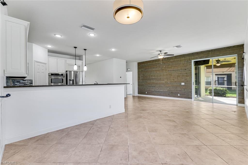 Open kitchen and living area with a white breakfast bar, tile floors, and a wood-plank accent wall.