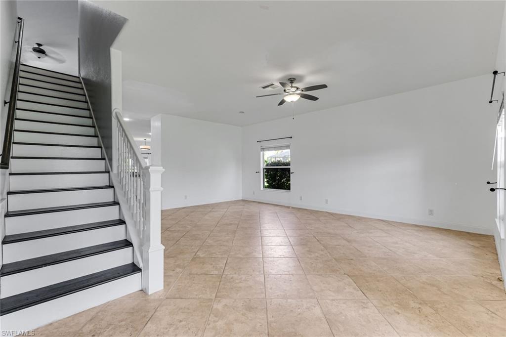 Vacant living room with beige tile floors and a staircase with dark treads and white railing.