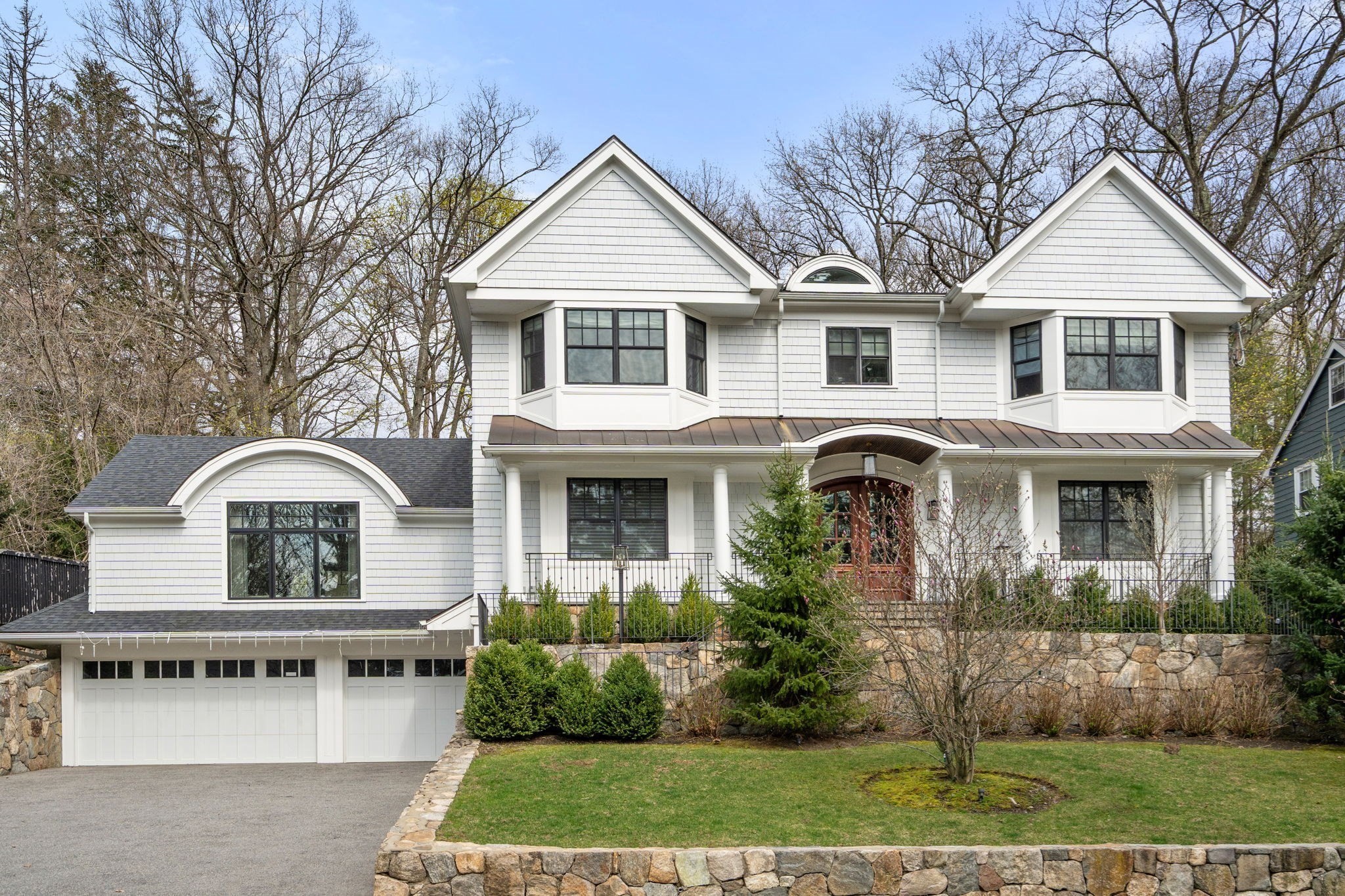 White shingle-style house with twin front gables, bay windows, an attached garage, and a stone-bordered lawn.