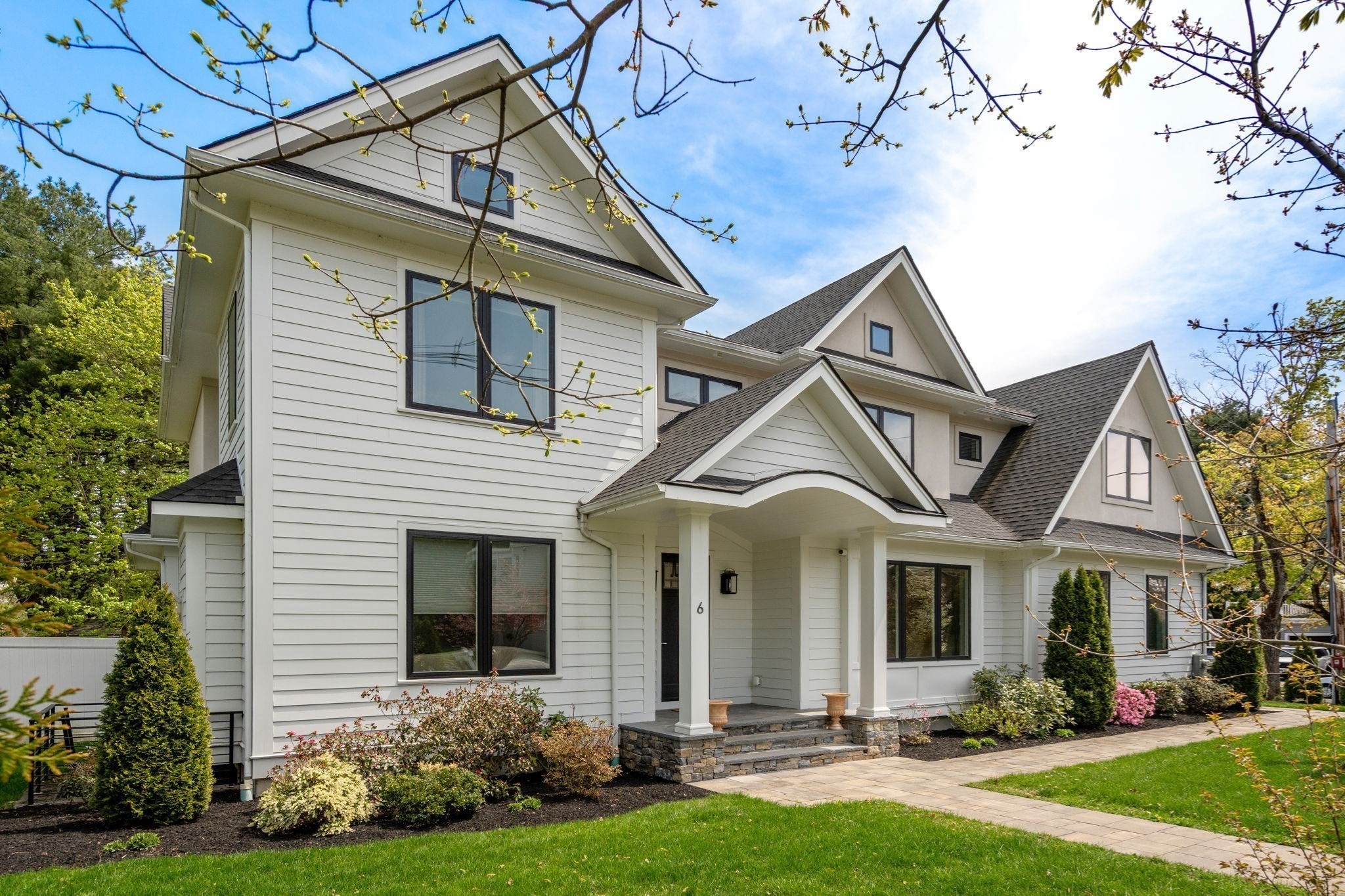 White multi-gabled house with a covered entry, landscaped shrubs, and a paved walkway.