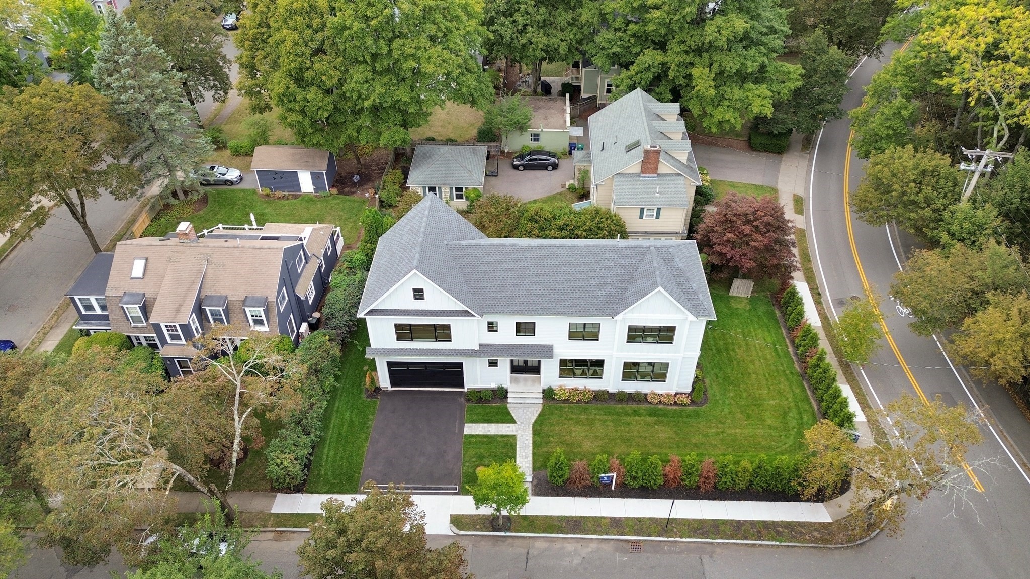 White two-story house with a gray gabled roof and landscaped corner lot, viewed from above.
