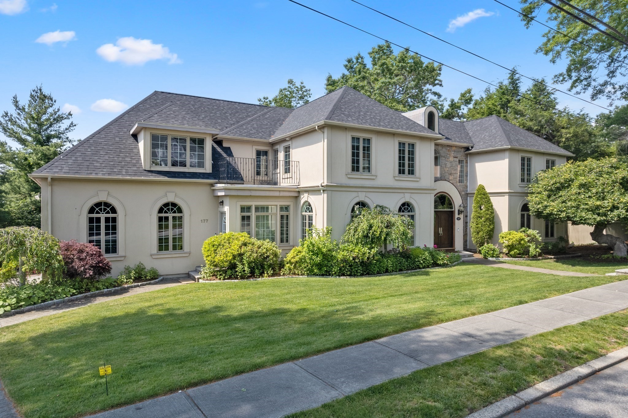 Two-story cream house with a gray shingle roof, arched windows, stone accents, and landscaped lawn.