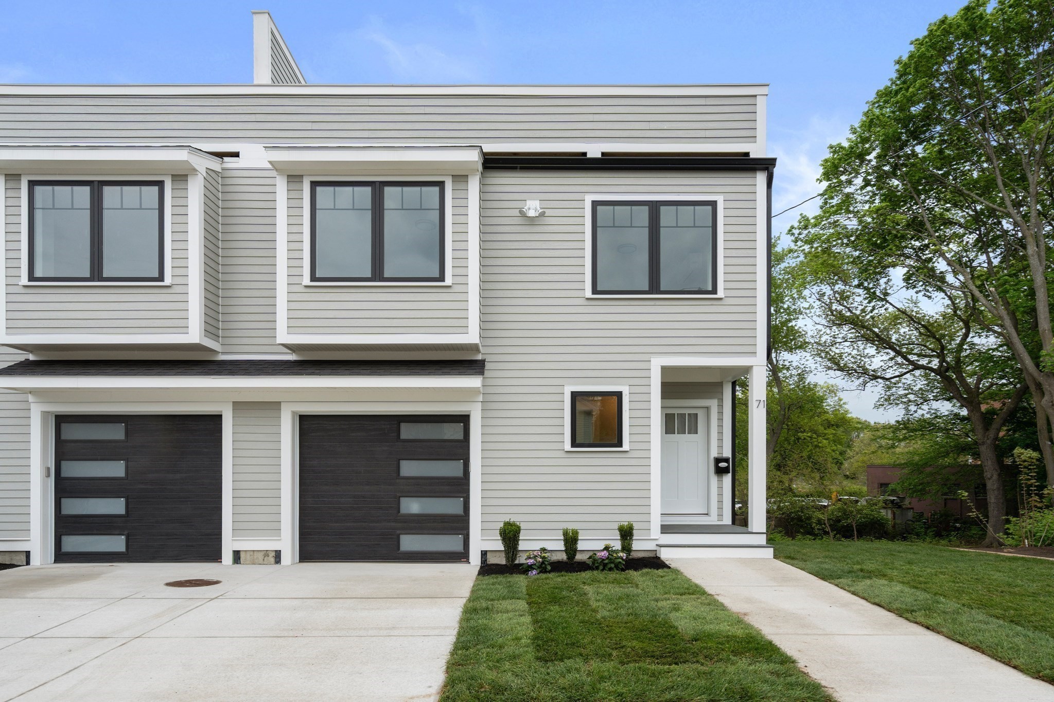 Modern light-gray home with two dark garage doors, a recessed entry, and a leafy yard.