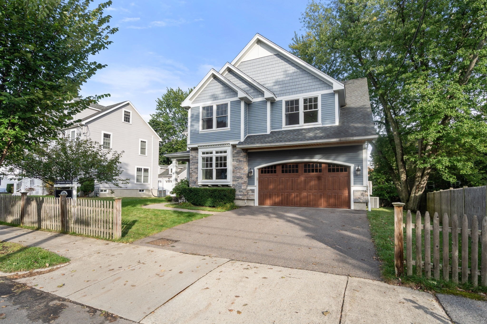 Blue-gray two-story home with stone accents, a brown double garage door, and a paved driveway.
