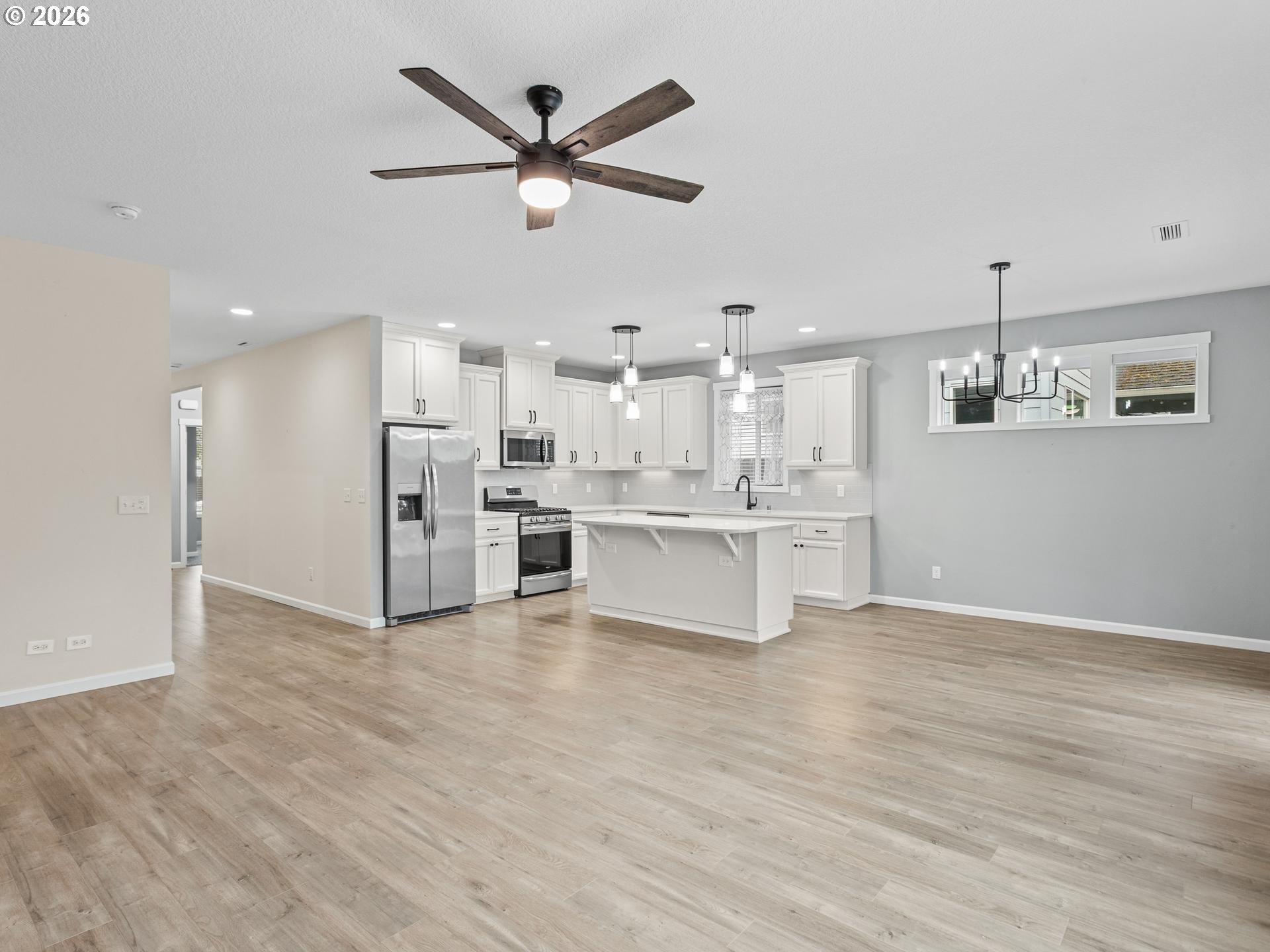 Open kitchen with white cabinetry, a central island, stainless steel appliances, and light wood-look flooring.