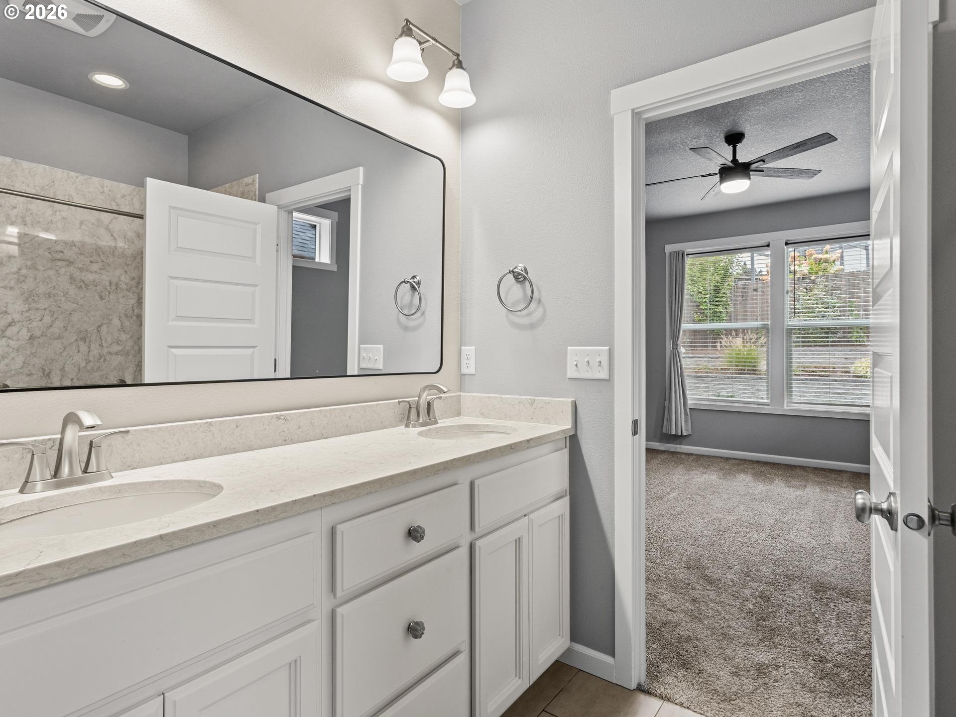 Bathroom double vanity with pale countertop and mirror, opening onto a carpeted bedroom.