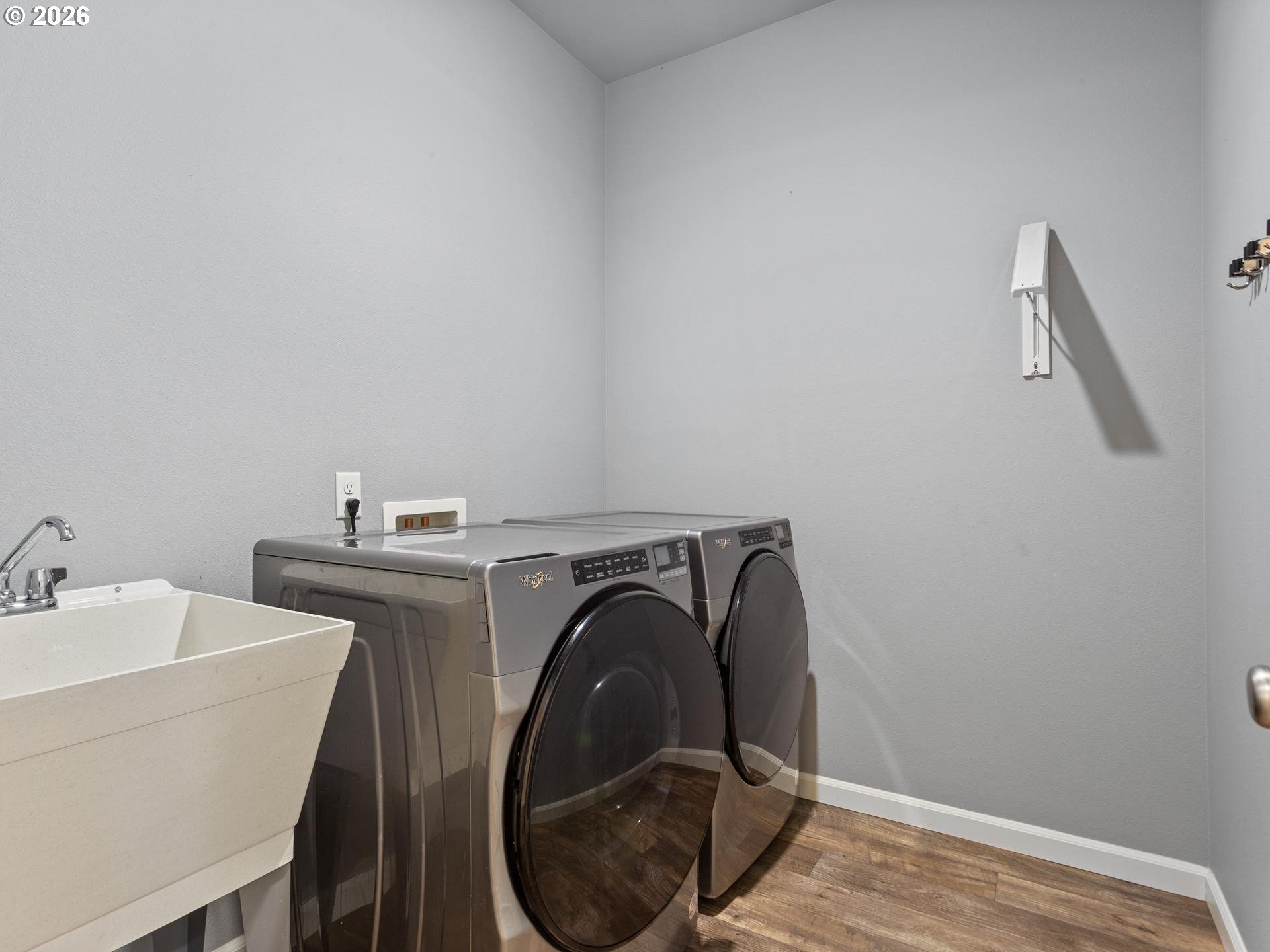 Laundry room with matching front-loading washer and dryer beside a white utility sink.
