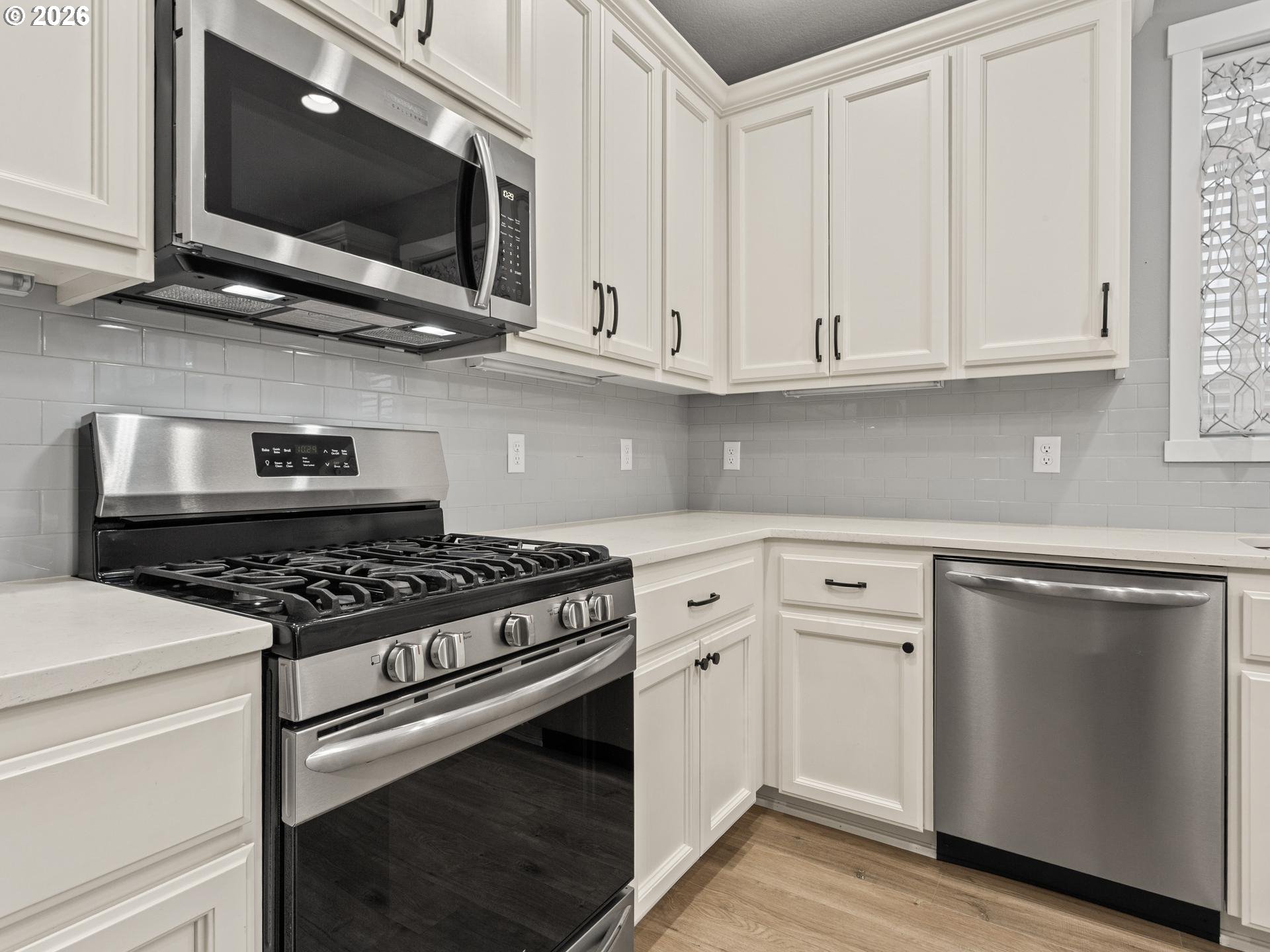 Kitchen with white cabinets, gray tile backsplash, stainless dishwasher, and gas range.