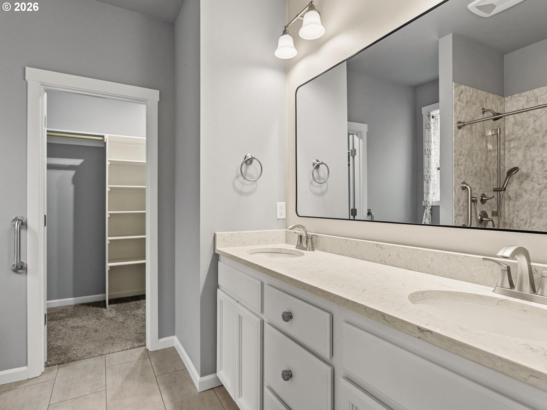 Bathroom with a long double vanity and large mirror, with a shower and shelved closet visible.
