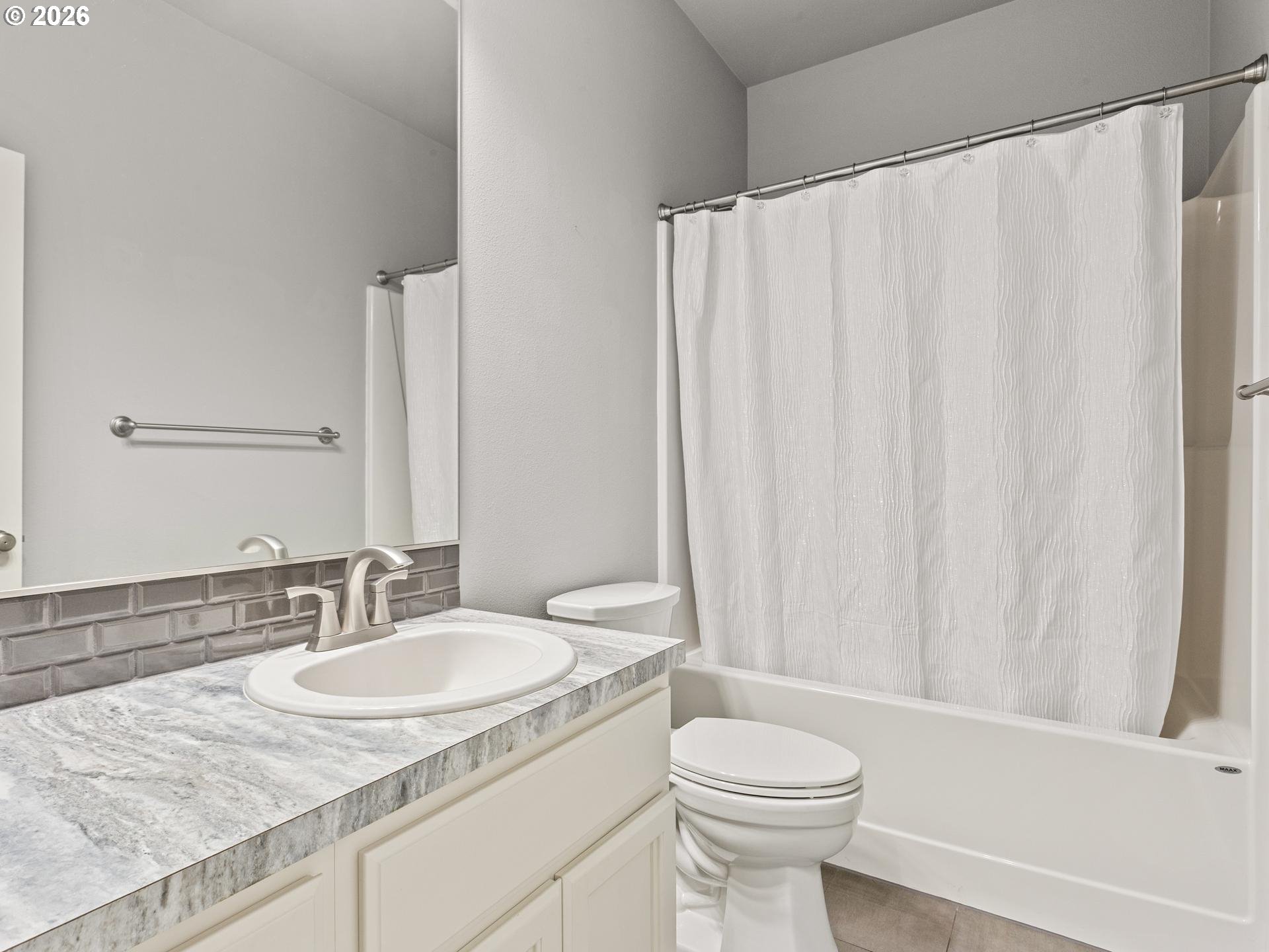 Bathroom with a gray-tiled vanity, white sink, toilet, and bathtub behind a textured shower curtain.