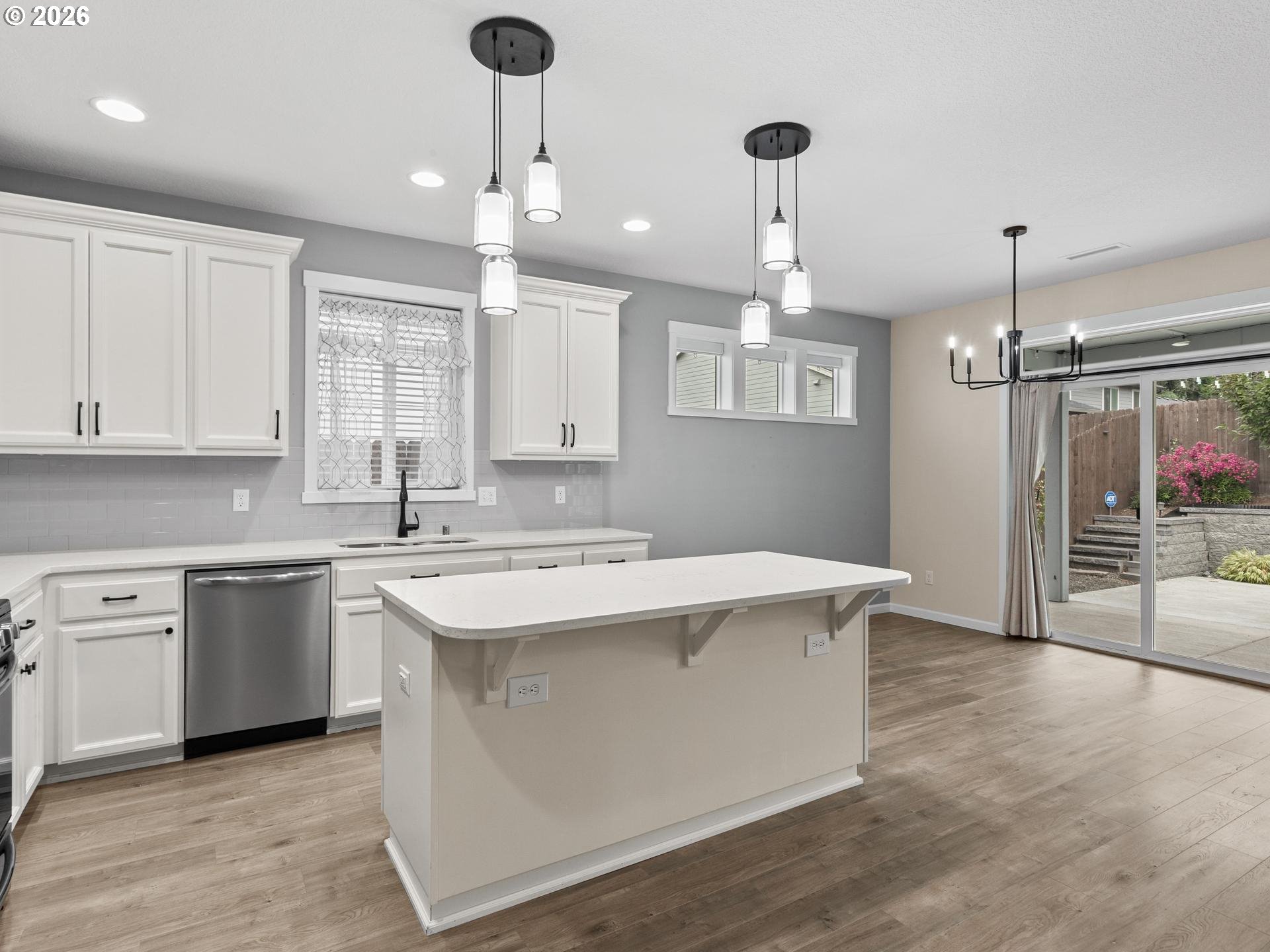 Kitchen with white cabinets, a large island, pendant lights, and sliding doors to a fenced patio.