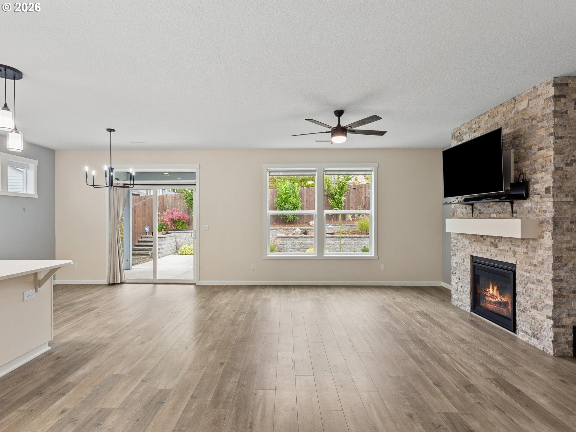 Empty living room with a stone fireplace, wall-mounted television, and sliding glass door to the patio.
