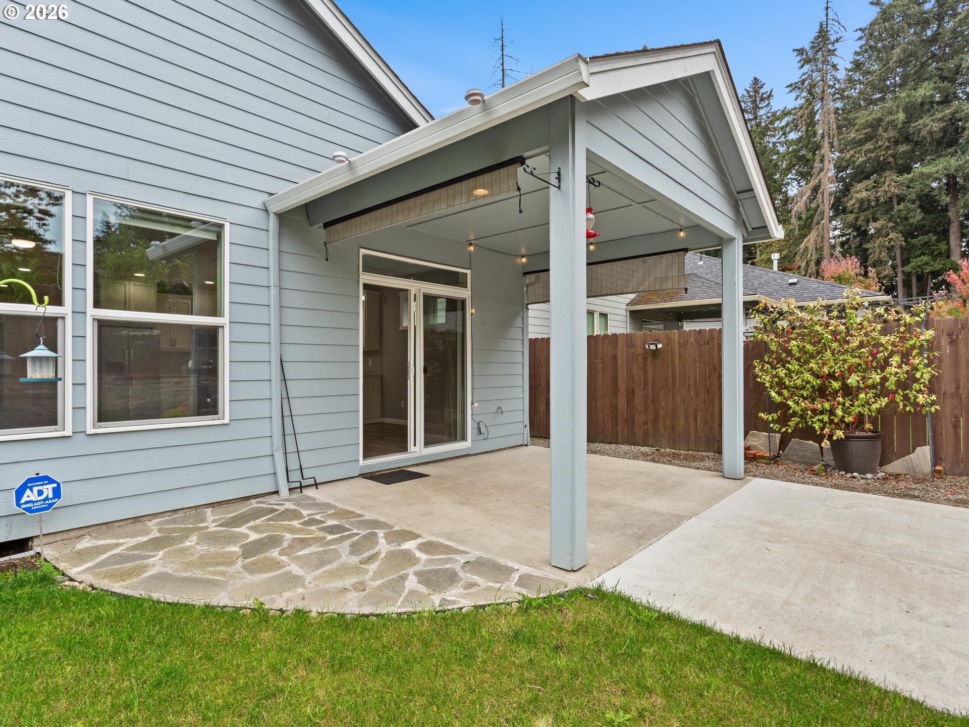 Covered backyard patio with a sliding glass door, stone paving, and a fenced garden.